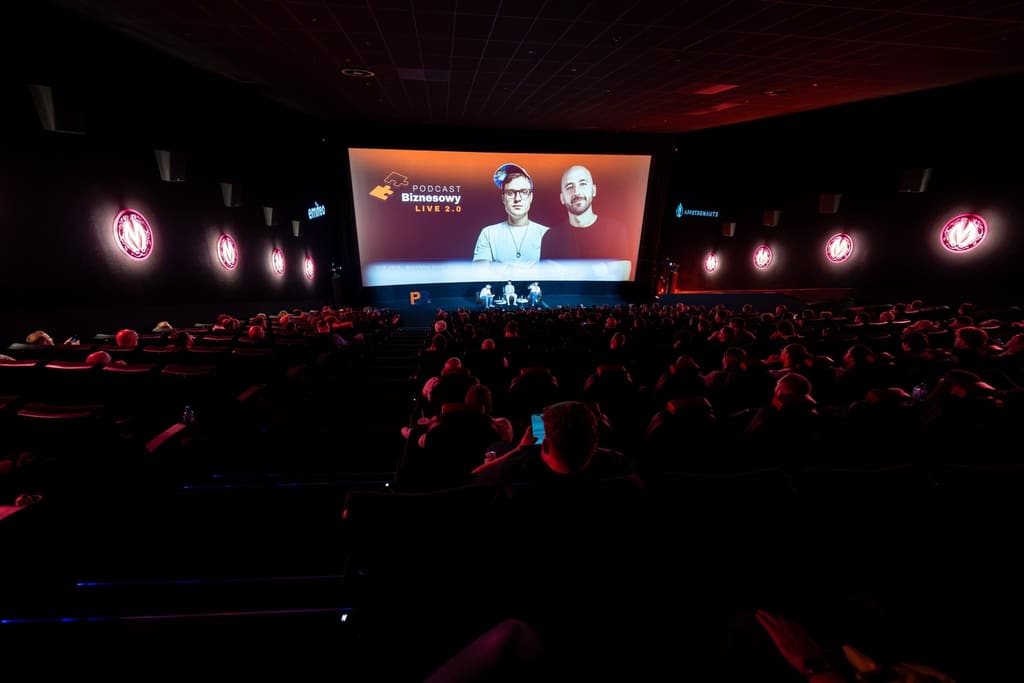 Pełna sala kinowa podczas PB Live 2, na ekranie Podcast Biznesowy LIVE